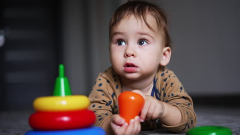 one year old child lies on the floor on his belly. cute kid holding a toy in little hands and taking it to a mouth. close up.