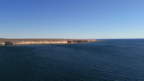experience a stunning aerial establishing shot over puerto madryn, argentina, showcasing the vast atlantic ocean and picturesque coastline under a clear, bright blue sky.
