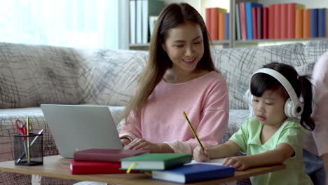 a beautiful asian mother busy working at home while looking after and teaching her children on a laptop computer