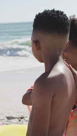 familia afroamericana sonriente usando crema solar en una playa soleada