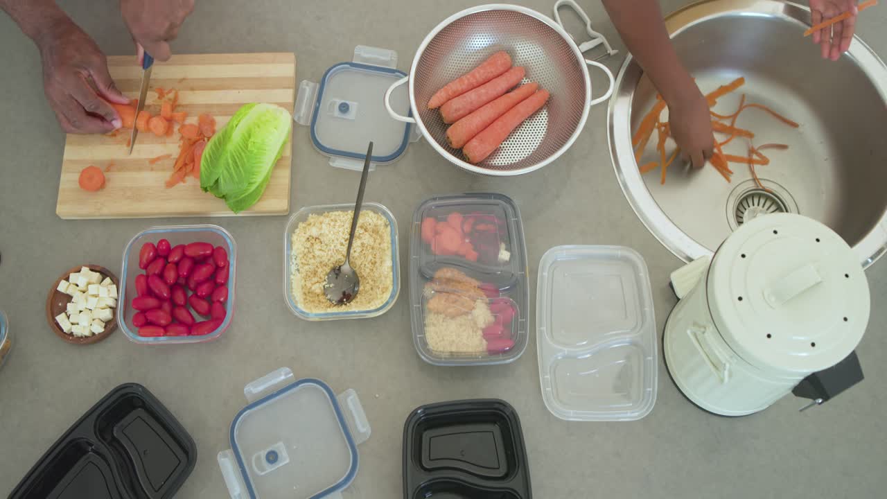 African male housemates with ingredients set chopping carrots on board, packing containers