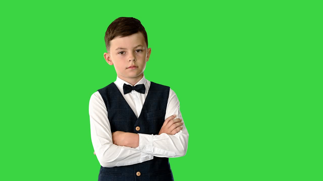 уверенный молодой мальчик в галстуке и жилете скрестил руки и положил руки в карманы, глядя на камеру на зеленом экране, хроматический ключ