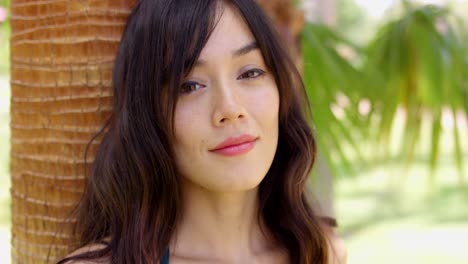 smiling young woman leaning against a palm