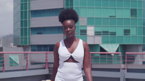 On-a-rooftop-with-the-city-skyline-in-view,-a-black-girl-wears-a-white-dress-walking