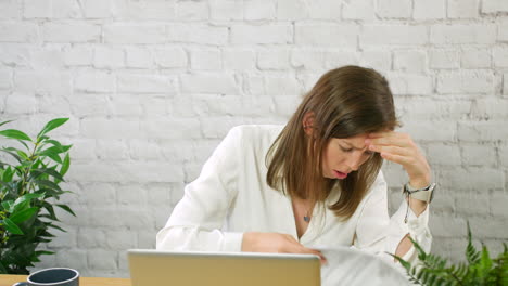 una mujer joven estresada y sobrecargada de trabajo con pilas de papeles en una oficina