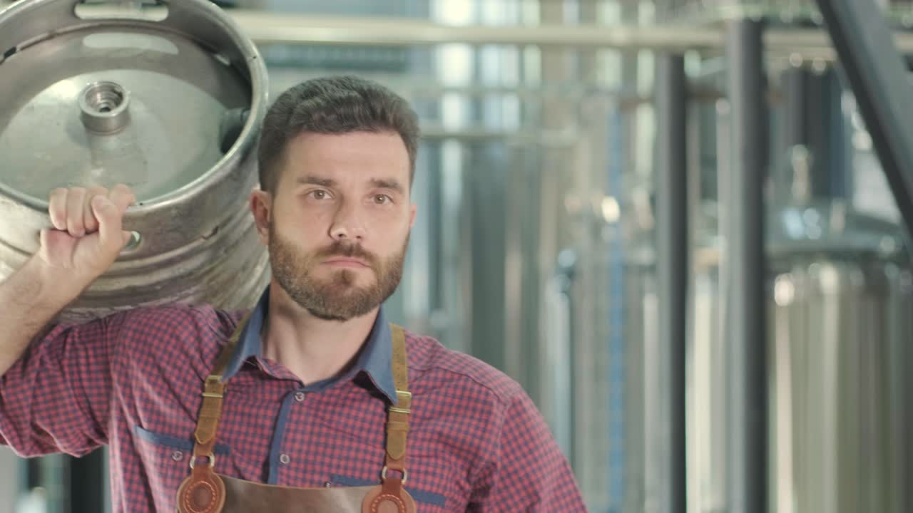 jonge brouwer met een leren schort draagt een vat ambachtelijk bier in een moderne brouwerij