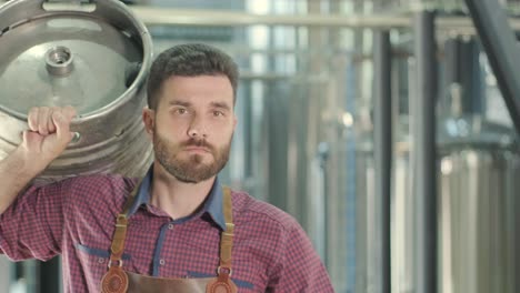 un joven cervecero con un delantal de cuero lleva un barril de cerveza artesanal en una cervecería moderna
