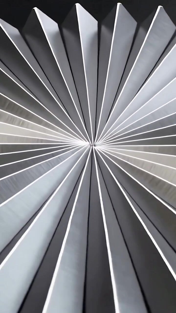 Vertical video: Pulling camera up centering pleated disc on dark table showing folds with rim light