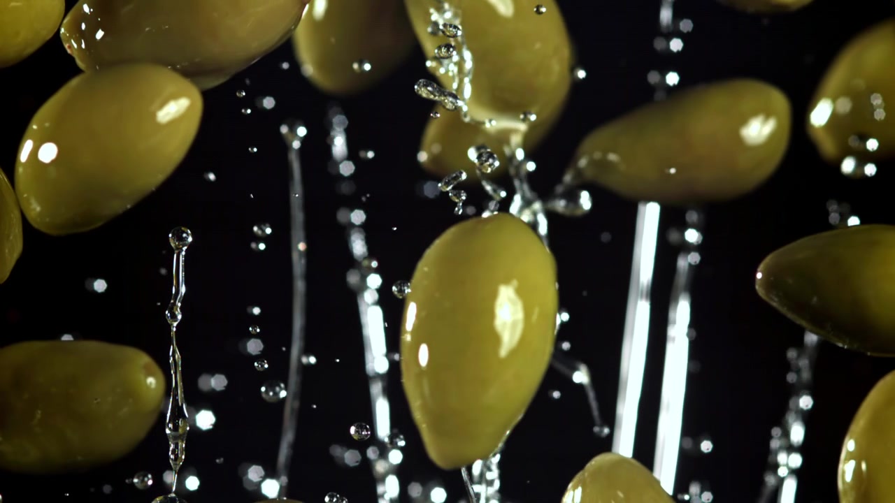 Olive verdi fresche che cadono con gocce d'acqua al rallentatore