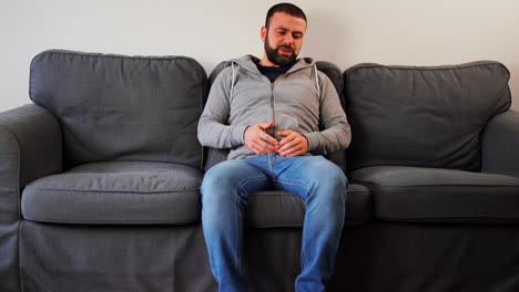 man having back ache, sitting on the sofa - wide shot