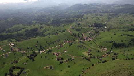 sirnea village in romania with green rolling hills and scattered houses, under a hazy sky, aerial view