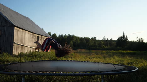 kid flips on a trampoline with an old barn in the background