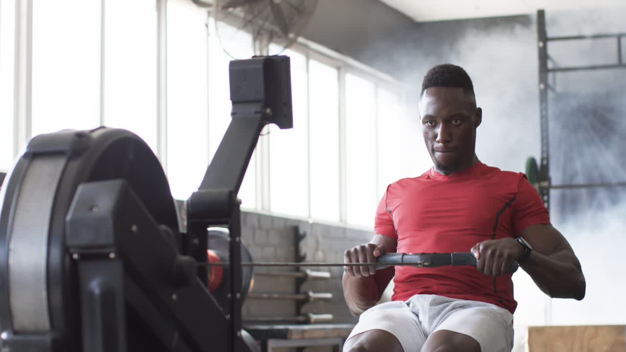 Young African American male, red shirt, white shorts, training on rowing machine