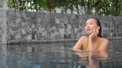 Close-up-of-a-woman-in-a-swimming-pool-leaning-on-her-leaning-her-chin-in-her-hand-is-backed-by-a-decorative-tile-wall