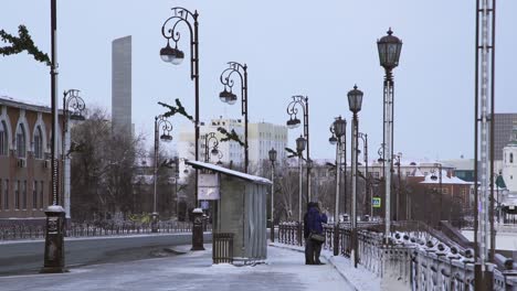 snowy city street with bus stop and people