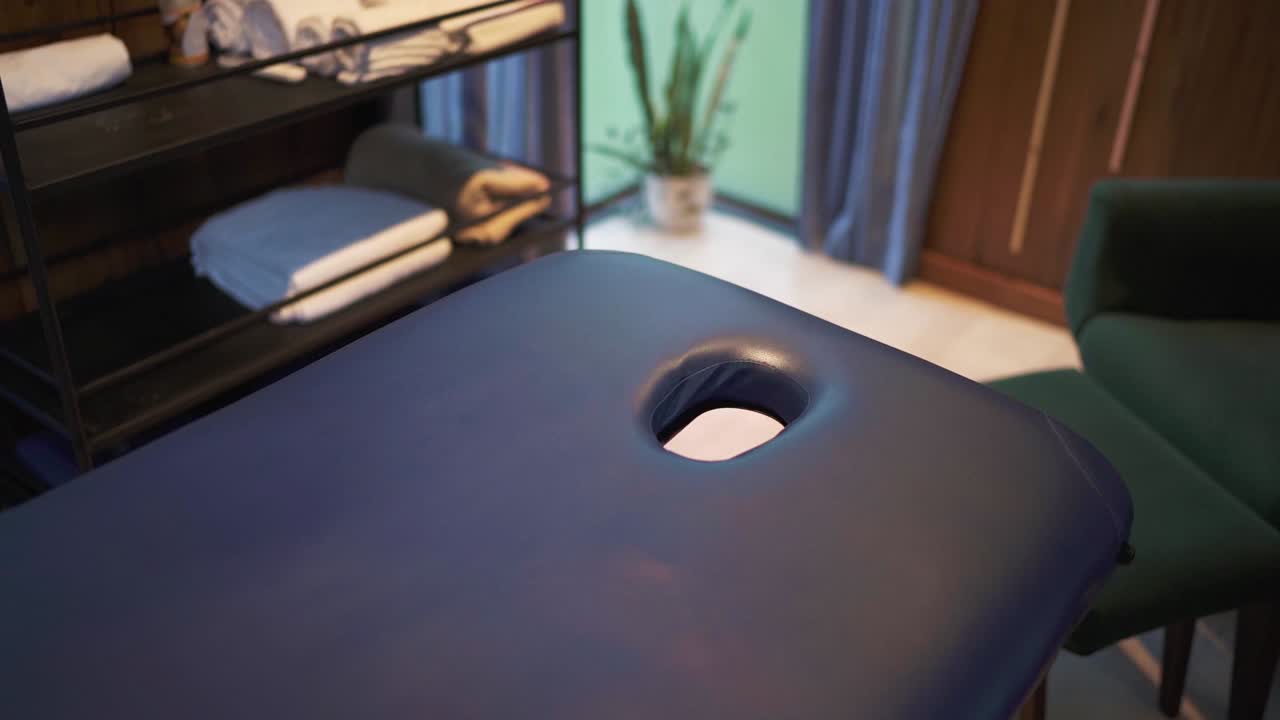 câmera de panorâmica lenta de mesa de massagem e quarto em hotel, argentina. paredes de madeira, cadeira verde e mesa de bandeja no local.