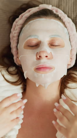 mujer agita las manos en el rostro acostada en la cama. mujer morena en bata de baño disfruta del tiempo después de los tratamientos de spa moviendo las manos en la cama suave en cámara lenta