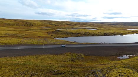 vista aérea de un coche conduciendo en la carretera en el paisaje pintoresco de islandia con lagos y praderas
