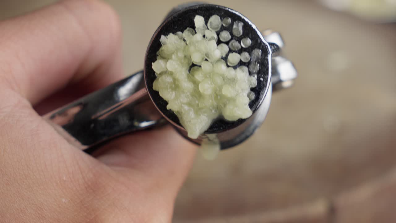 Hand Squeezing Out Minced, Crushed, Garlic Using A Small Garlic Pressing Tool.