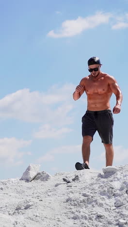 muscular man walking on white canyon. strong shirtless man in black glasses going down in a slow motion on mountain under clear sky. vertical video