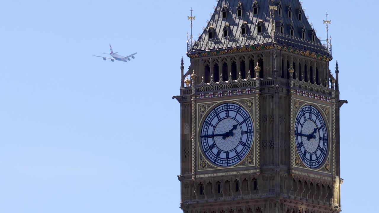 A commercial airplane flies past the iconic clock tower against a clear blue summer sky