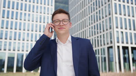 Portrait-shot-of-young-smiling-business-man-talking-on-phone-outdoors