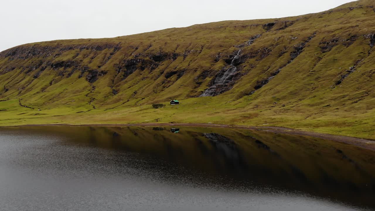 Lavvinkel flyfoto i høy hastighet av en liten hytte på fjellet ved siden av en liten foss og en uberørt elv