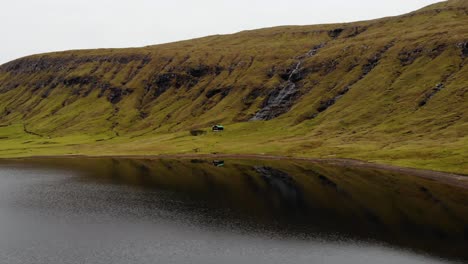 Aerial-low-angle-high-speed-of-small-cottage-in-the-mountains-next-to-a-small-waterfall-and-an-unspoiled-river