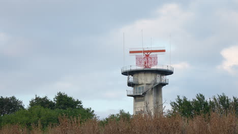 rotating radar system mounted on concrete tower with cloudy sky in the background