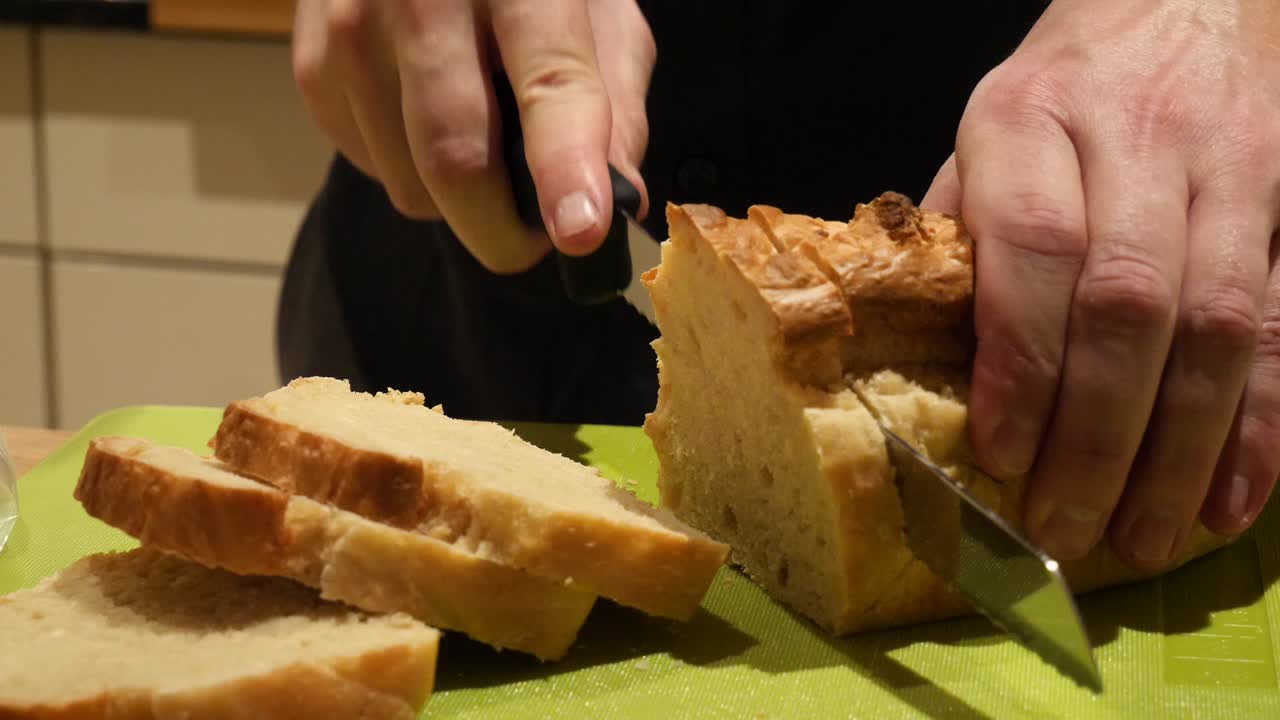A white male hand model is slicing fresh baked toast bread on a green cutting board in slow motion
