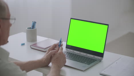 retiree man is communicating online using laptop with video chat green screen on pc for post-production
