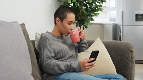 Woman-using-smartphone-and-having-a-coffee-in-living-room