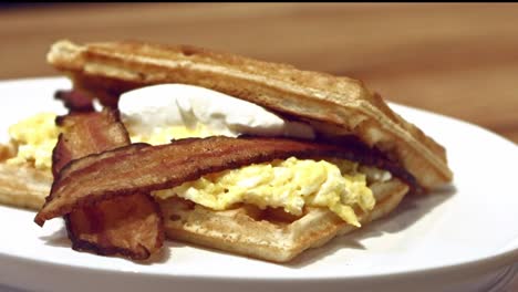 un sándwich de desayuno hecho con gofres, huevos revueltos, tocino y queso crema vista aislada giratoria