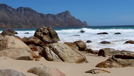 waves crashing into a rocky beach, low shot with mountain in background