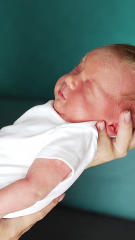 newborn in white bodysuit is slowly waking up. dad's hand tickling baby's belly. close up. vertical video