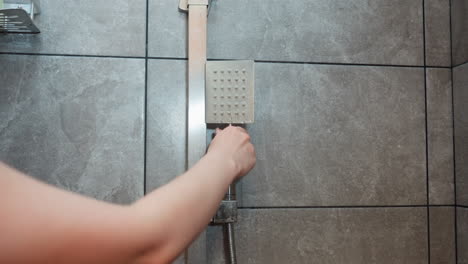 close up of woman hand placing shower head onto wall mount following leg rinse as water drips from head onto tiled bathroom floor capturing subtle drip motion and calm bath moment