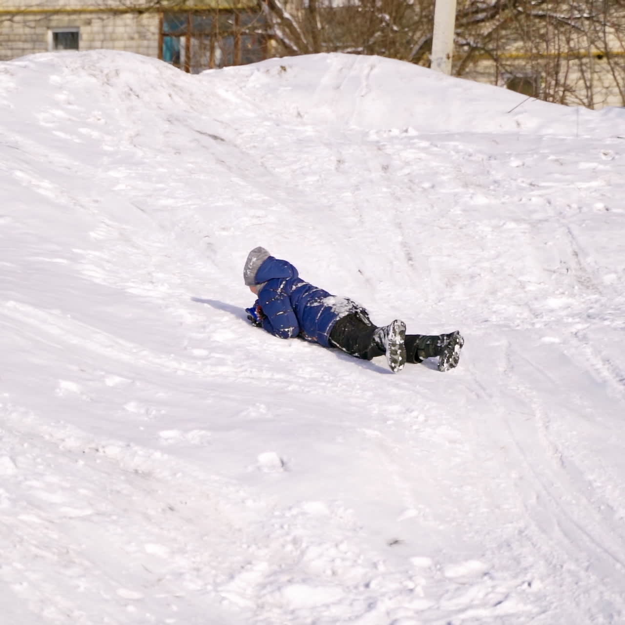 Joyful boy lying happily on snow. Happy kid having fun in snow in the city park. Winter holidays. Slow motion.