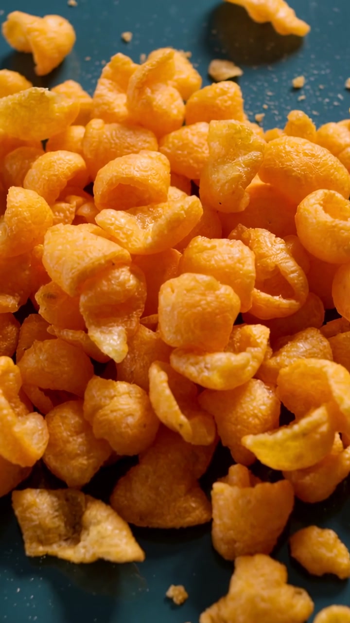 Vertical video: Starting camera filming pile of cheese puffs on blue plate in kitchen, with crumbs
