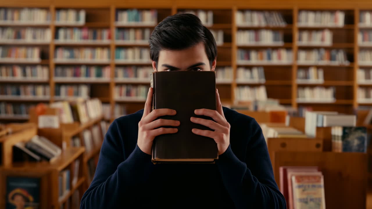 Jeune homme jetant un coup d'œil par-dessus un livre dans une bibliothèque