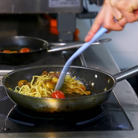 cooking and stirring the spaghetti with red tomatoes and mushrooms in the frying pan. video from a side