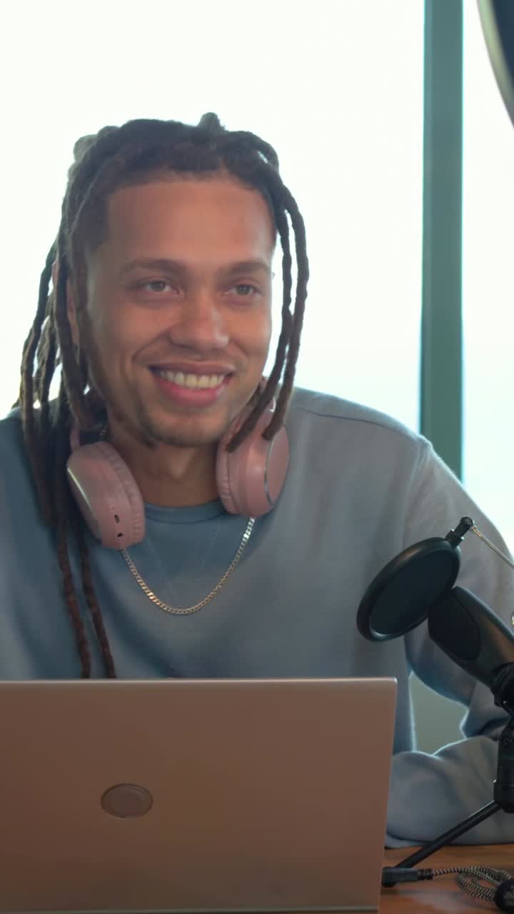 Male creator seeing laptop message, smiling, typing, leaning to mic, recording podcast waveform