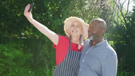 feliz pareja diversa tomando una selfie en el jardín