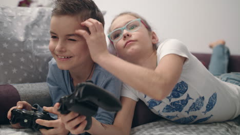 Siblings-enjoy-video-game-at-home.-Girl-close-eyes-boy.-Kids-have-fun-together