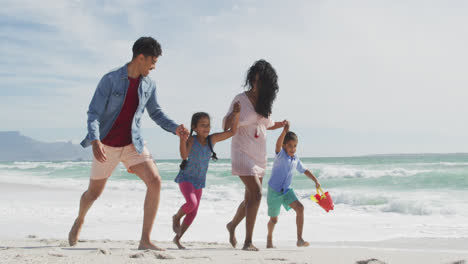 happy hispanic mother, father, son and daughter walking and playing on beach