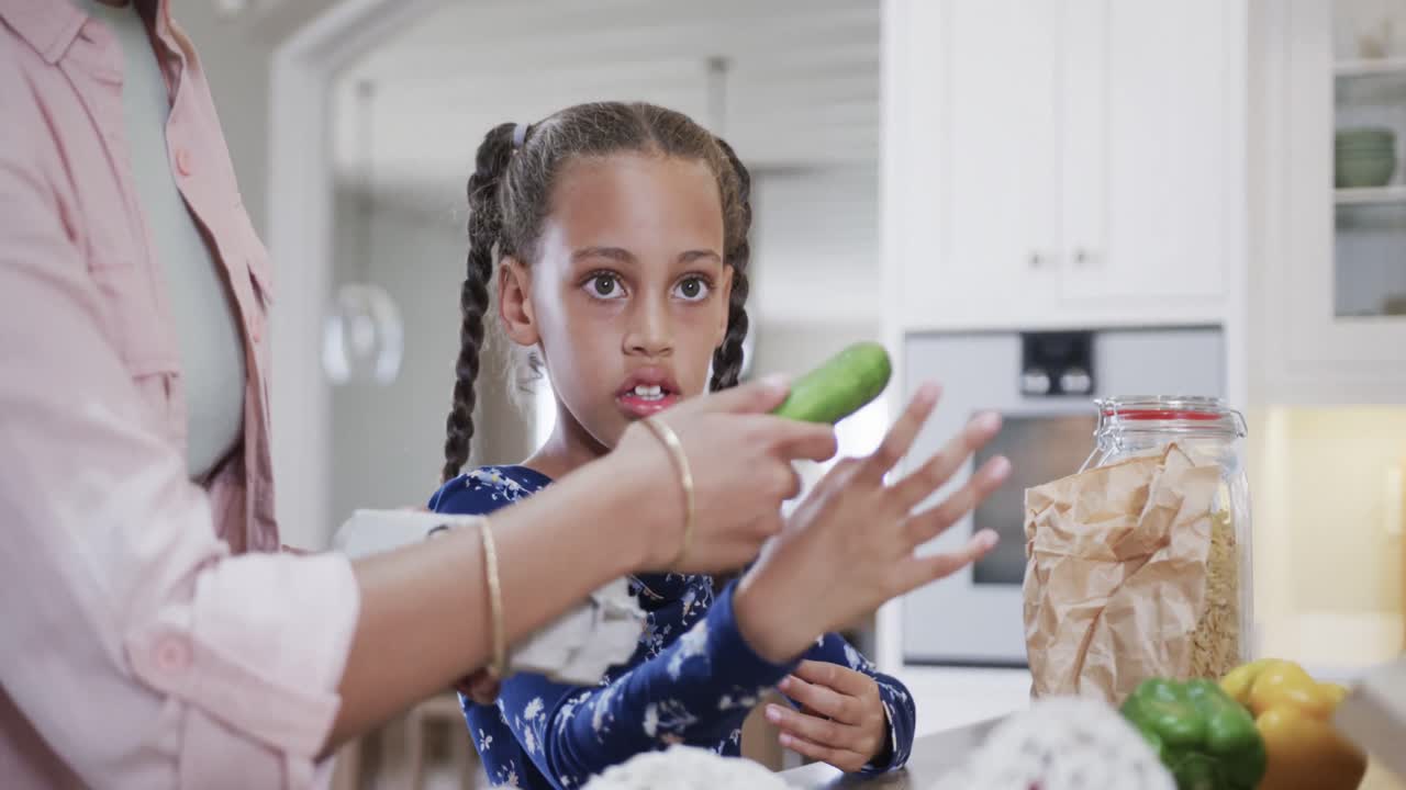 Biracial mother and daughter unpacking shopping in kitchen, slow motion