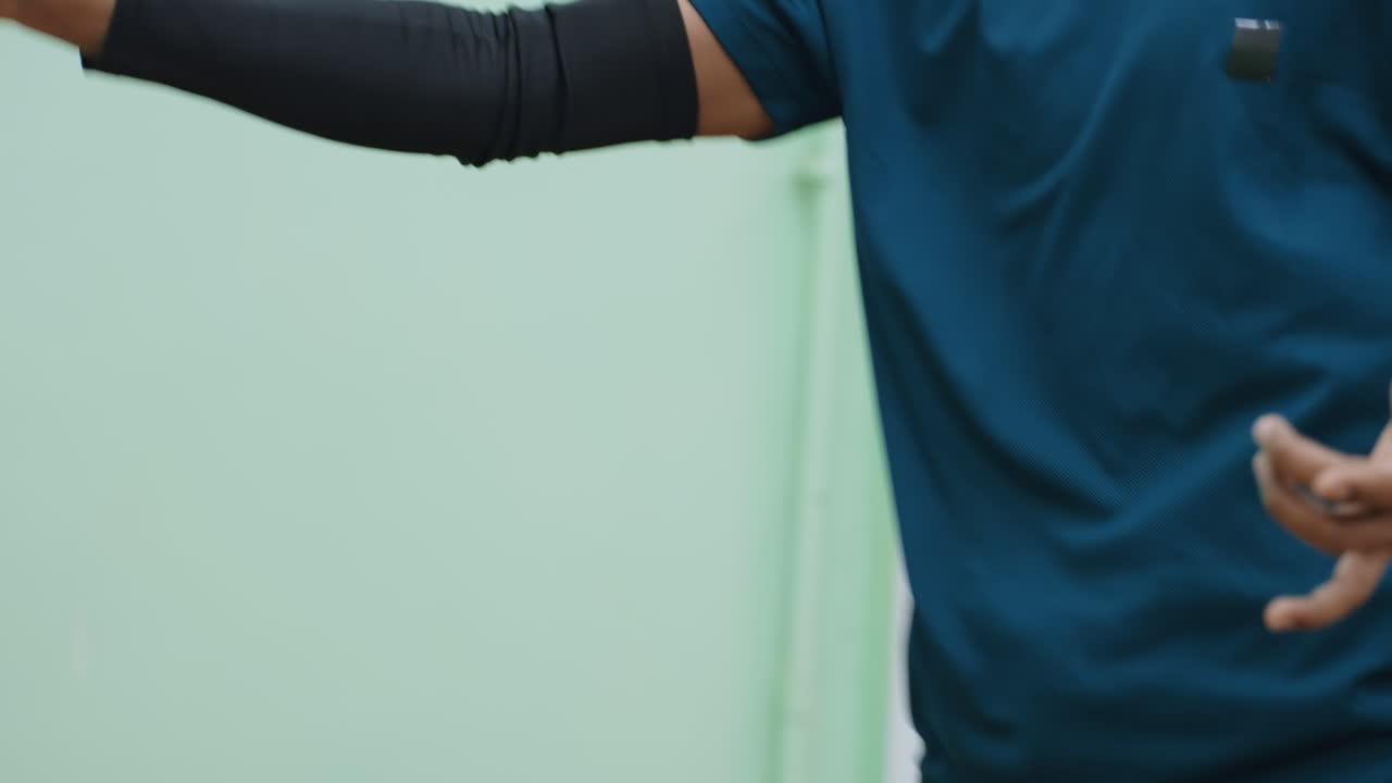 Close up of tennis player in blue sportswear holding racket while training indoors, focused on improving movement, strength, agility, and precision during intense practice session in sports facility