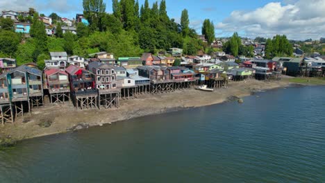 Coloridas-Casas-De-Madera-Del-Delta-Sobre-El-Agua-De-Mar-De-La-Isla-En-La-Patagonia-Chilena,-Paisaje-Aéreo-De-Drones-De-Barrio,-Horizonte-En-Verano