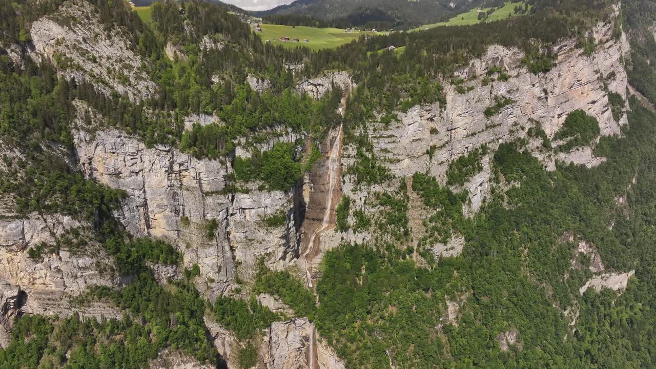 Seerenbachfälle in Switzerland, where multiple powerful waterfalls cascade down towering, verdant cliffs. Lush green forests cling to the steep rock faces, contrasting with the light gray stone