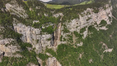 seerenbachfälle in switzerland, where multiple powerful waterfalls cascade down towering, verdant cliffs. lush green forests cling to the steep rock faces, contrasting with the light gray stone
