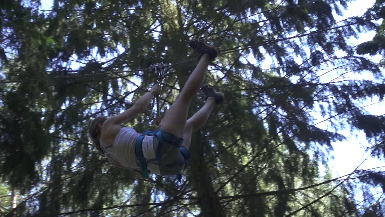 mujer joven en equipo de seguridad moviéndose en la cuerda con carabina en el parque de escalada